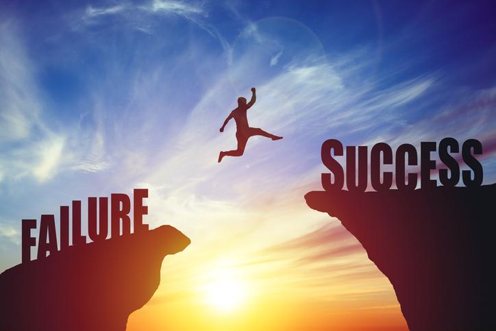 A man leaps between rocks against a blue sky, one marked 'failure' and the other 'success'.