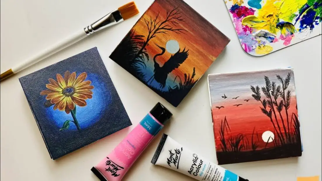 Acrylic paintings arranged beside two tubes of colorful acrylic paint and a paintbrush, against a clean white background