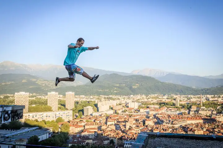 A man practicing parkour, suspended in mid-air with a blue sky in the background.