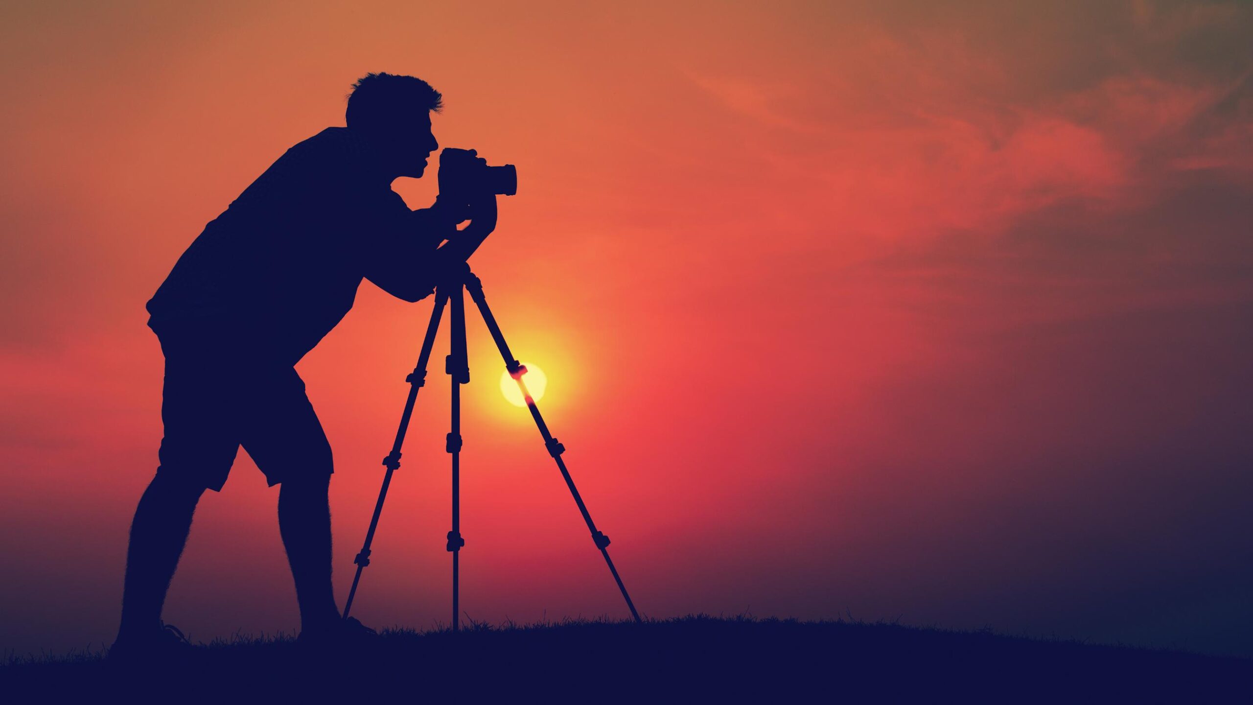 A silhouette of a photographer capturing a stunning sunset on the horizon