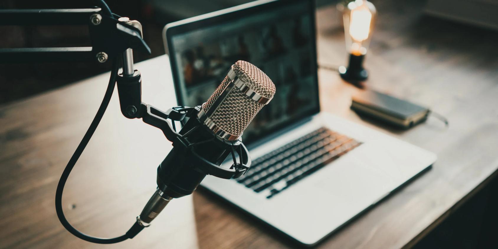 A microphone stands prominently in the foreground, accompanied by a laptop resting on a table in the background. 