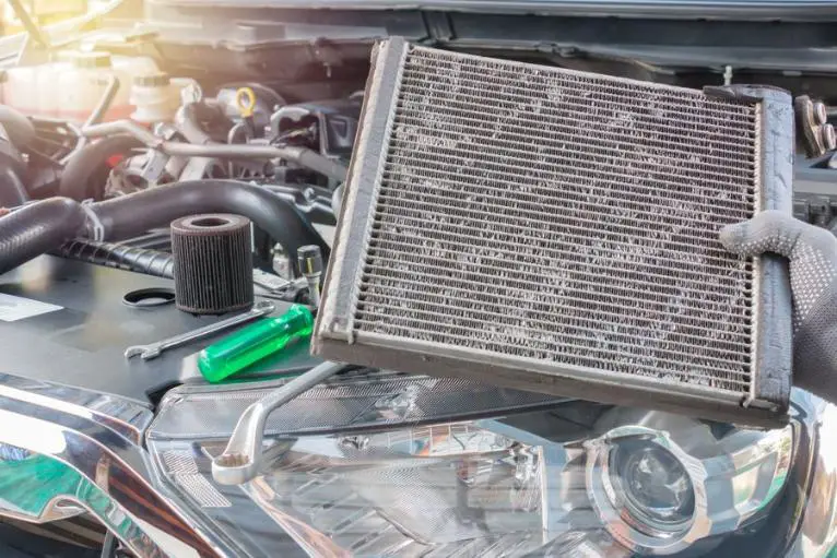A person holding a car radiator against the backdrop of a car interior, showcasing automotive maintenance and repair.
