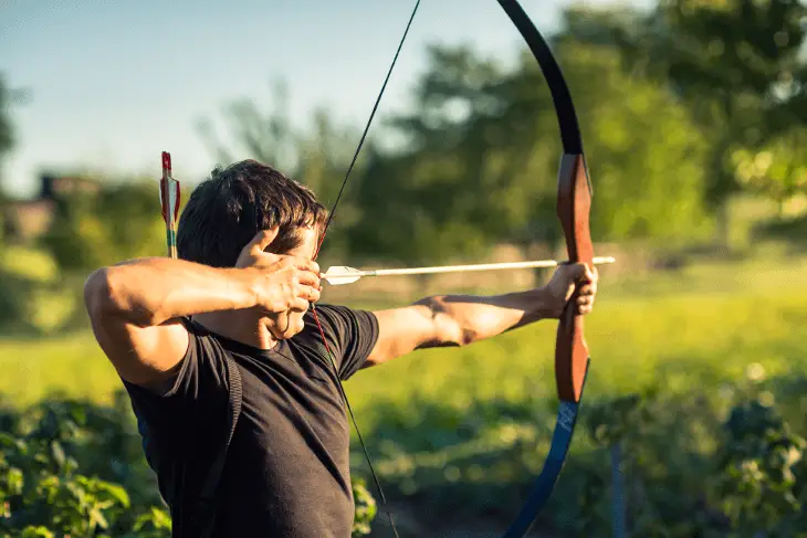A boy engaged in archery, holding a bow with a focused stance.