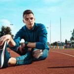 Man runner stretching legs preparing run training stadium tracks doing warm up