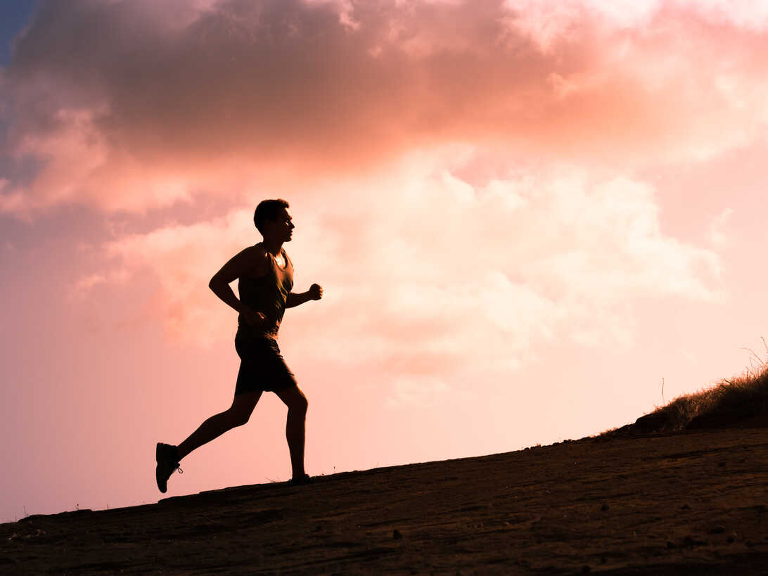 Silhouette of a man in motion, running atop an elevation against the captivating horizon