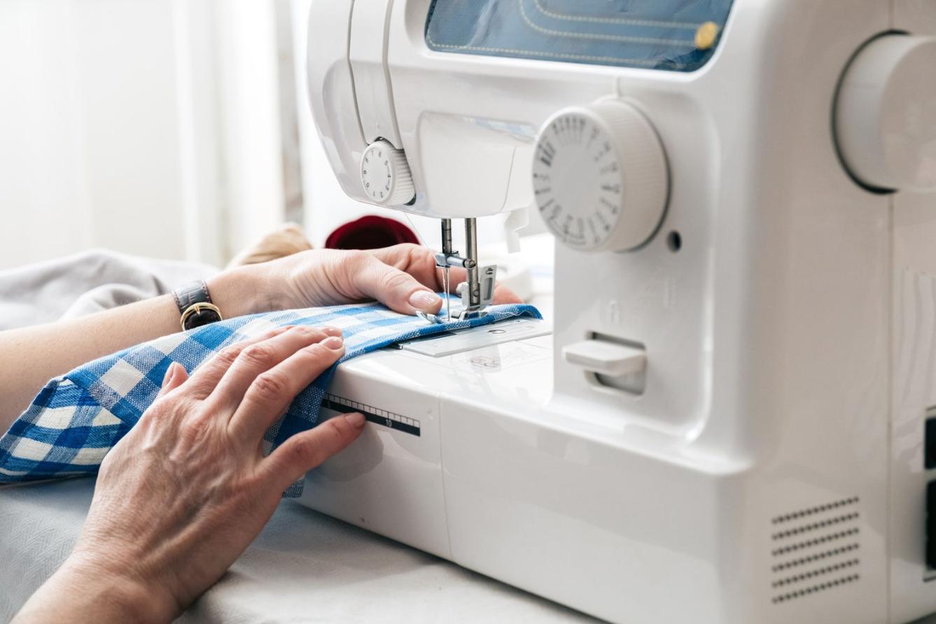 A female hand pulling a piece of fabric through a sewing machine foot