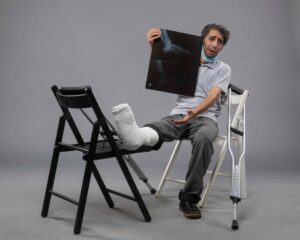 Young Male Sitting on Chair With Broken Foot Holding X-Ray