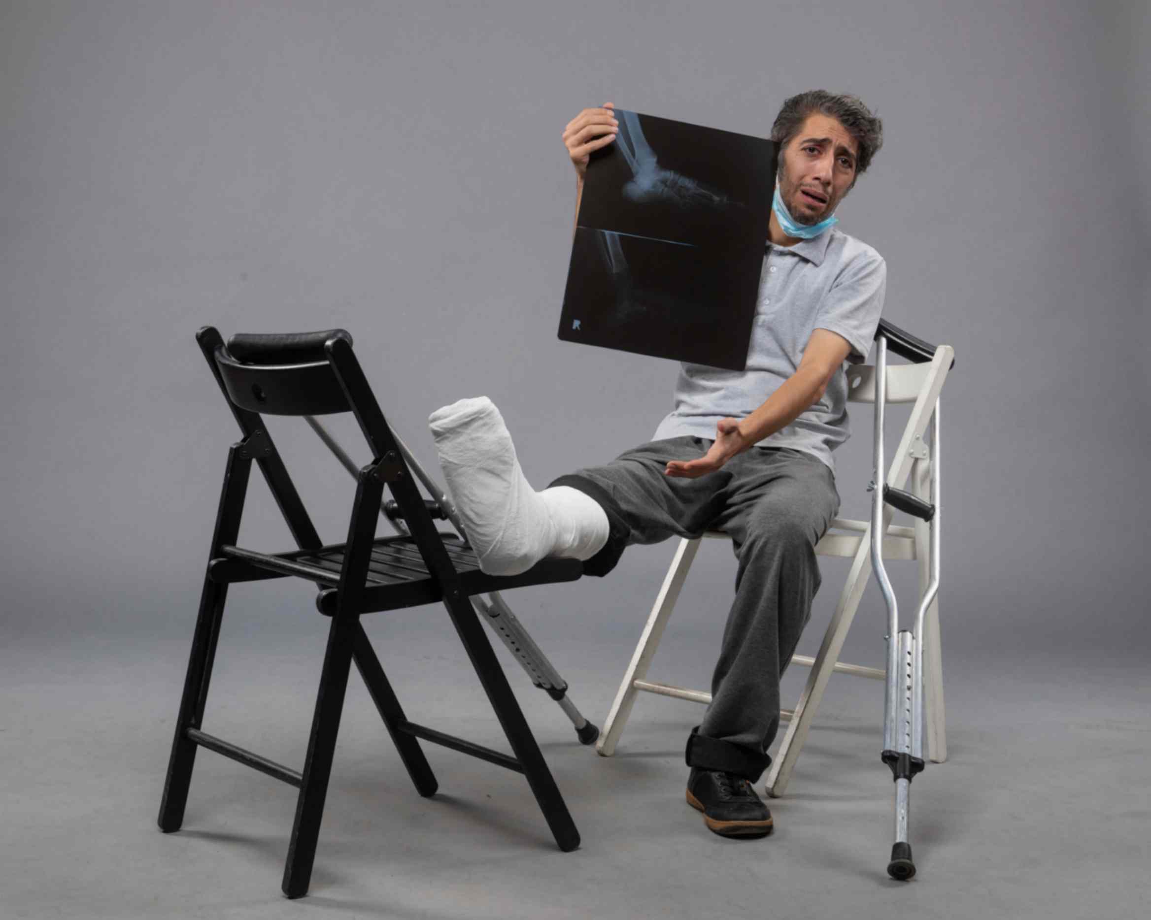 Young Male Sitting on Chair With Broken Foot Holding X-Ray