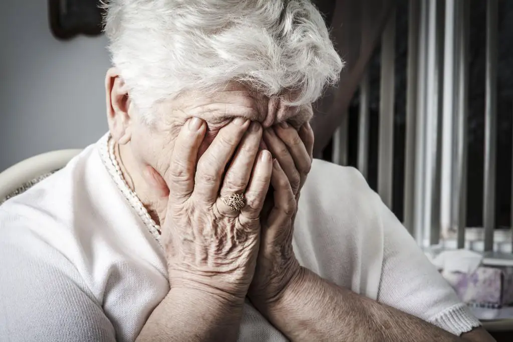 A saddened elderly woman has covered her face with her hands, expressing feelings of distress or despair.