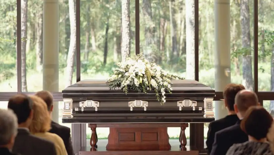 A coffin is placed in front of a funeral gathering.