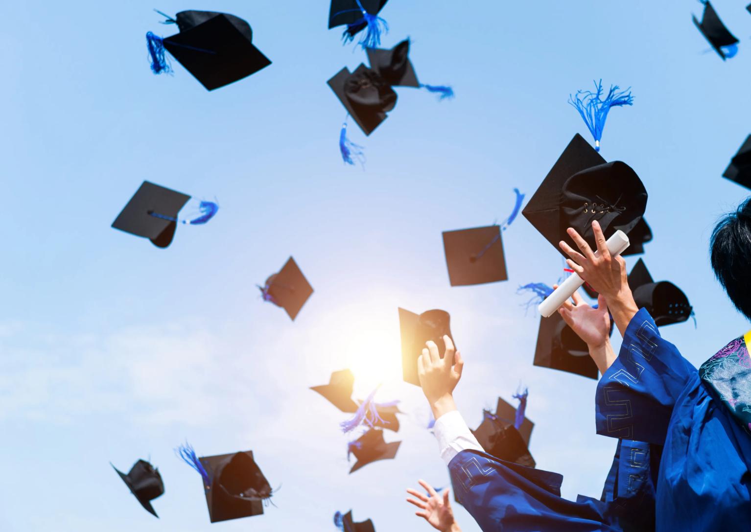 Tossed graduation caps against a blue sky.
