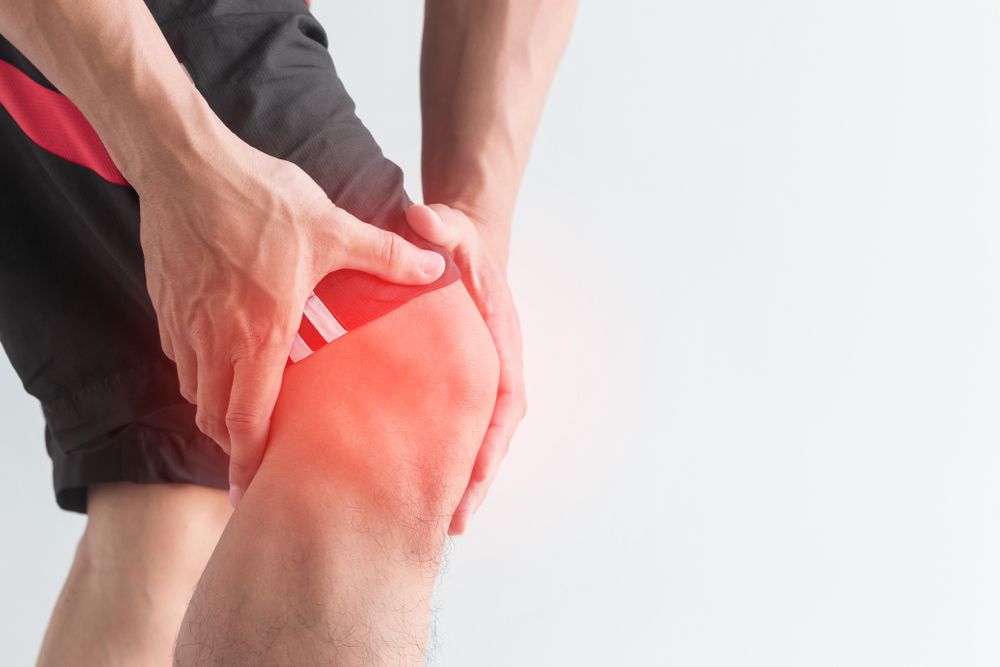 A man in black shorts is holding his hurt knee, highlighted by the presence of redness around the affected knee area.