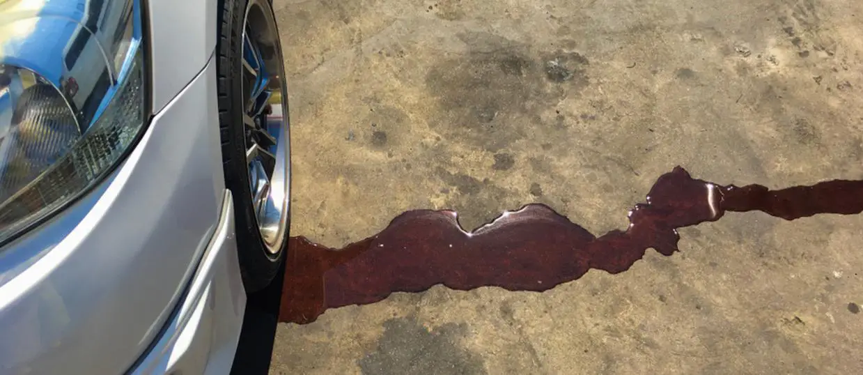 A white vehicle with a noticeable leak, forming a puddle on one side. 