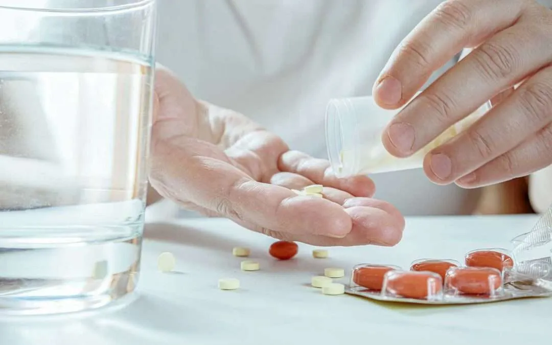 Hands of a man carefully taking pills out of a medicine box, with a glass of water placed beside the medications