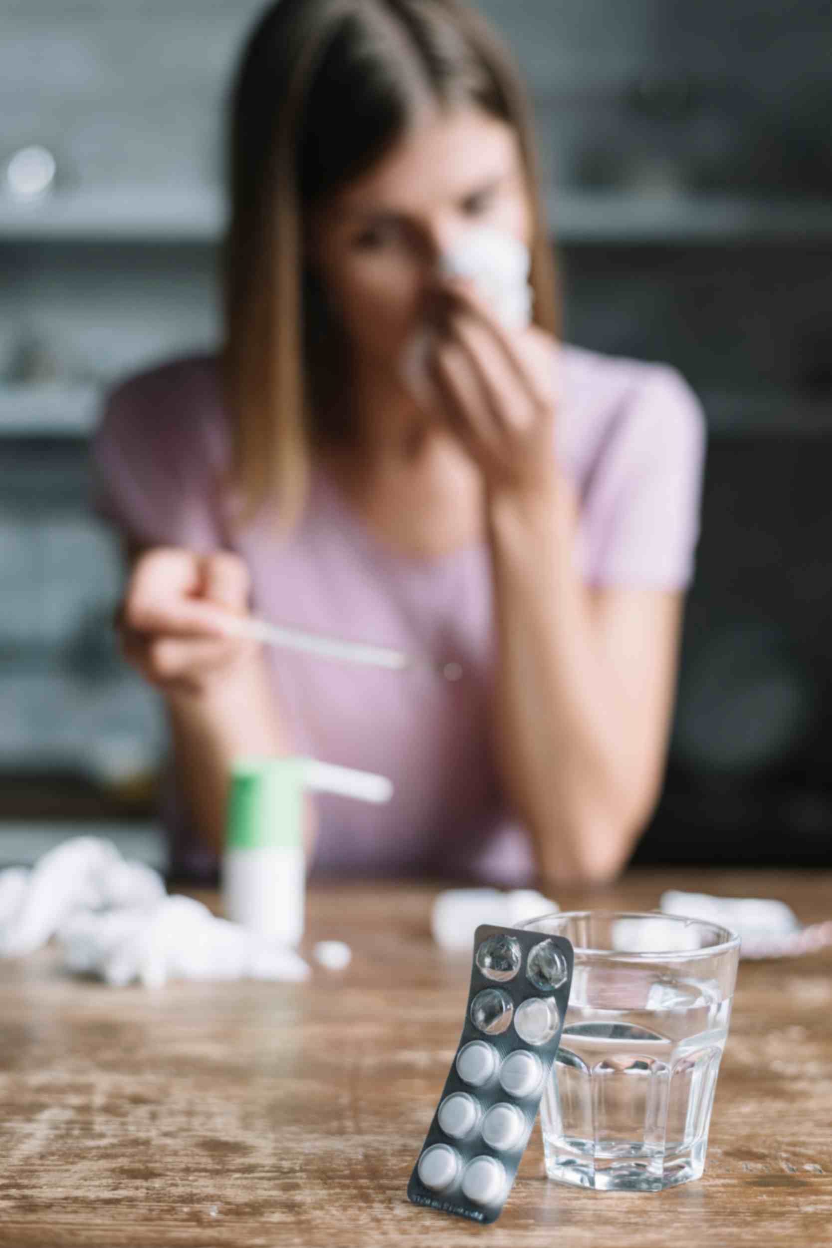 A sick girl sitting on a chair with a glass of water and medicines placed in front of her