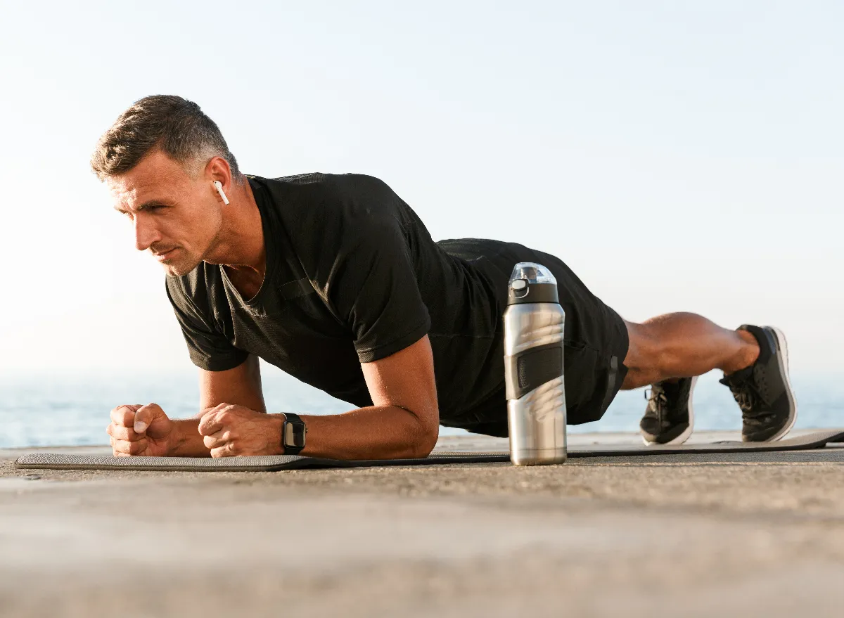 A fit man performing a forearm plank exercise with a water bottle placed aside.