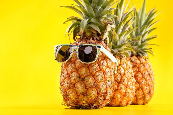 Three pineapples lined up, the first one wearing sunglasses, placed against a yellow background