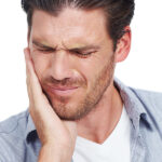A man holding their hand against the side of their face, indicating toothache or dental discomfort.