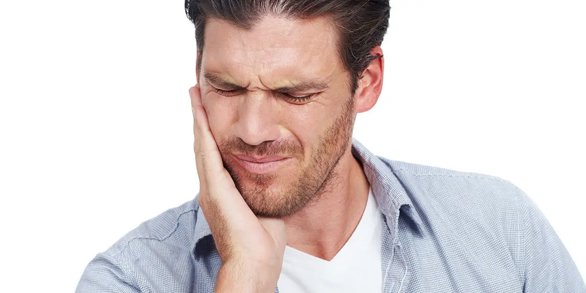 A man holding their hand against the side of their face, indicating toothache or dental discomfort.
