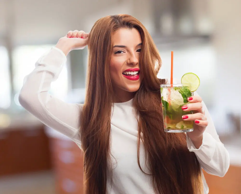 woman smiling while holding glass with lime