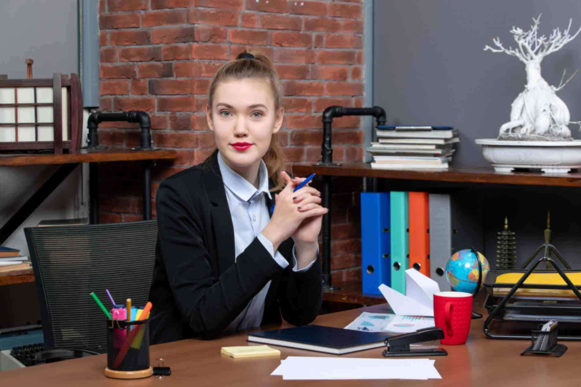 A businesswoman, holding a pencil and sitting in her office posing for the camera