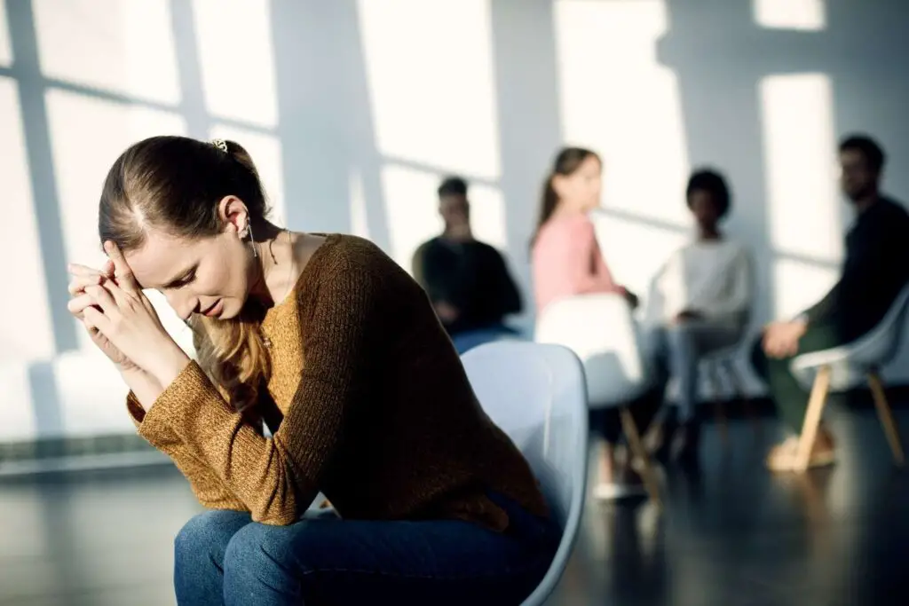 young-sad-woman-sitting-apart-from-attenders-group-therapy