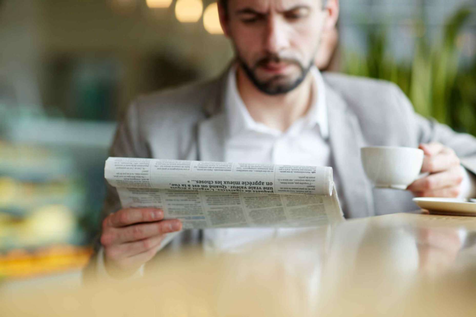 A person reading newspaper while sipping tea