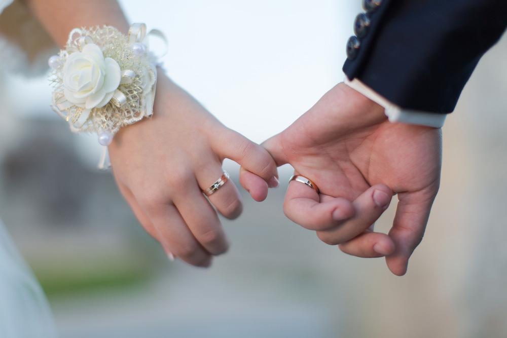 The interwoven pinky fingers of a married couple.