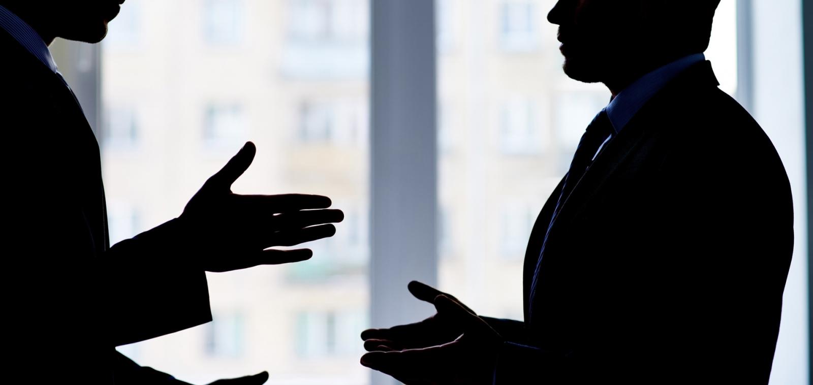 Silhouette of two men in conflict, shown in an office setting.