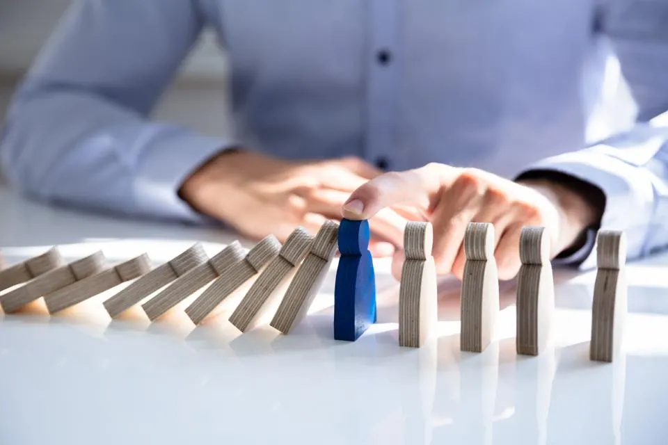 Small humanoid stops falling dominos, blue figure protects others.