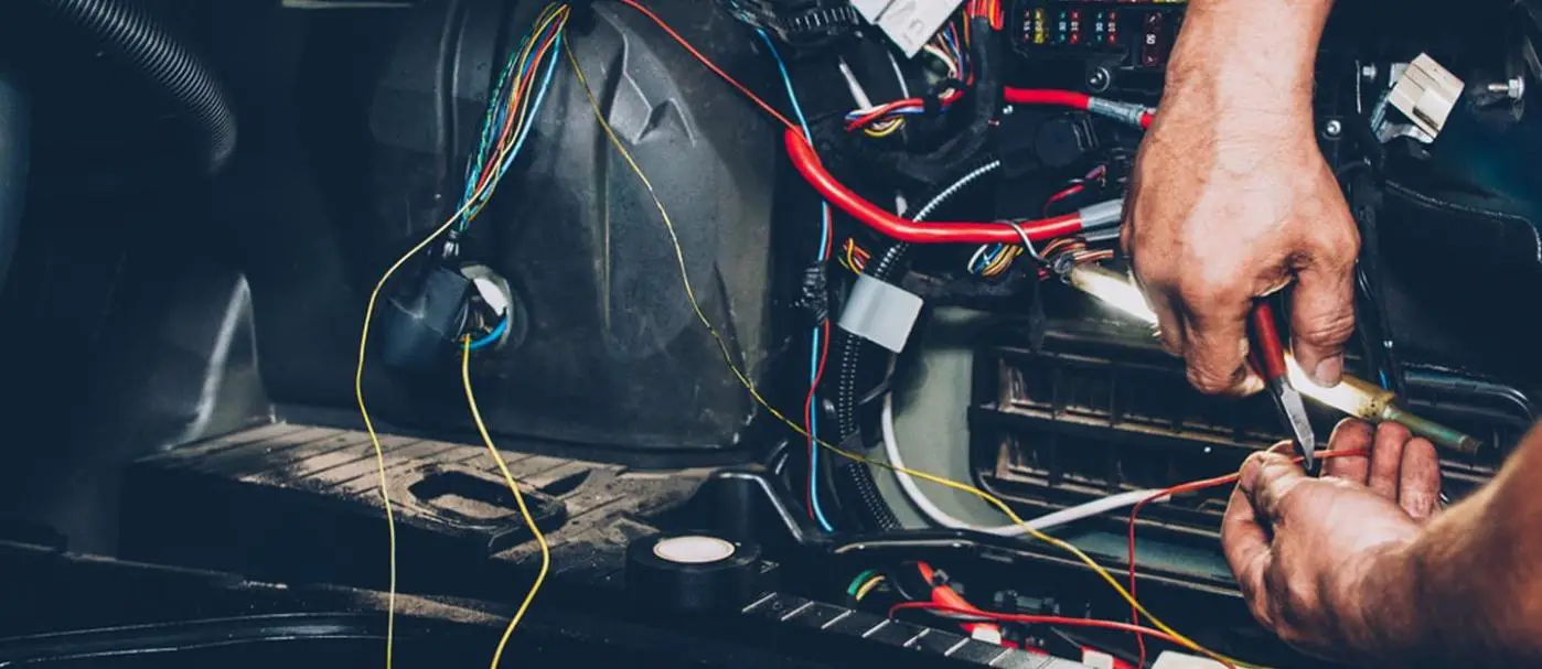 A man's hand fixing electrical issues in a car 