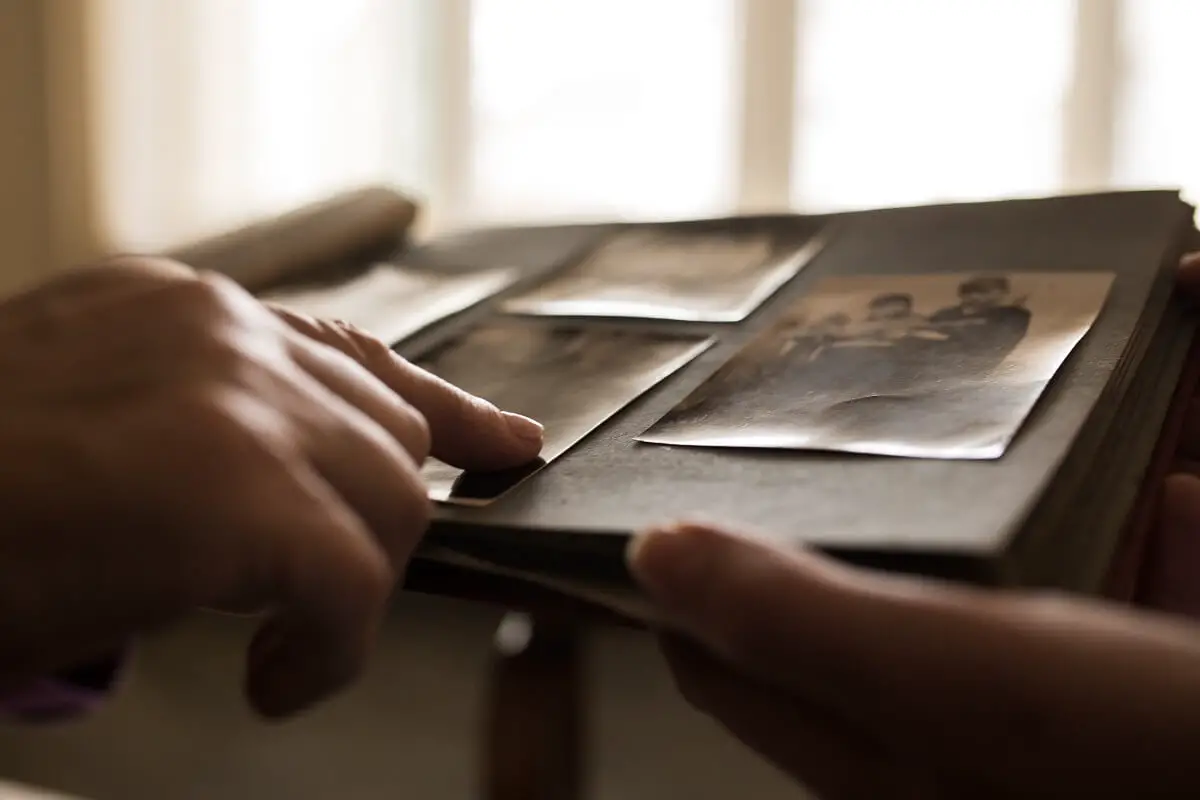 A woman's hand points to an old image in a photo album, while showing it to another person.