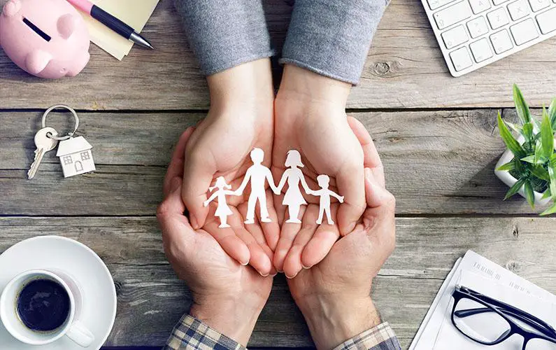 A paper-cut silhouette of a family held delicately in a woman's hand, cradled within the reassuring grasp of a man's hand, symbolizing love, support, and unity.