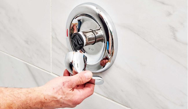 A man's hand inspecting a shower valve by removing the knob