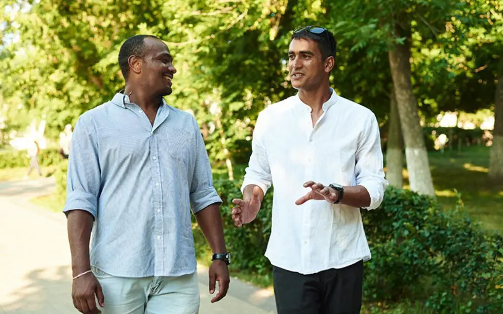Two men talking cheerfully while walking in a park.