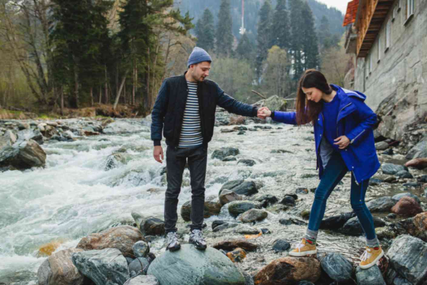 A man and woman holding hand moving through rocks over flowing river