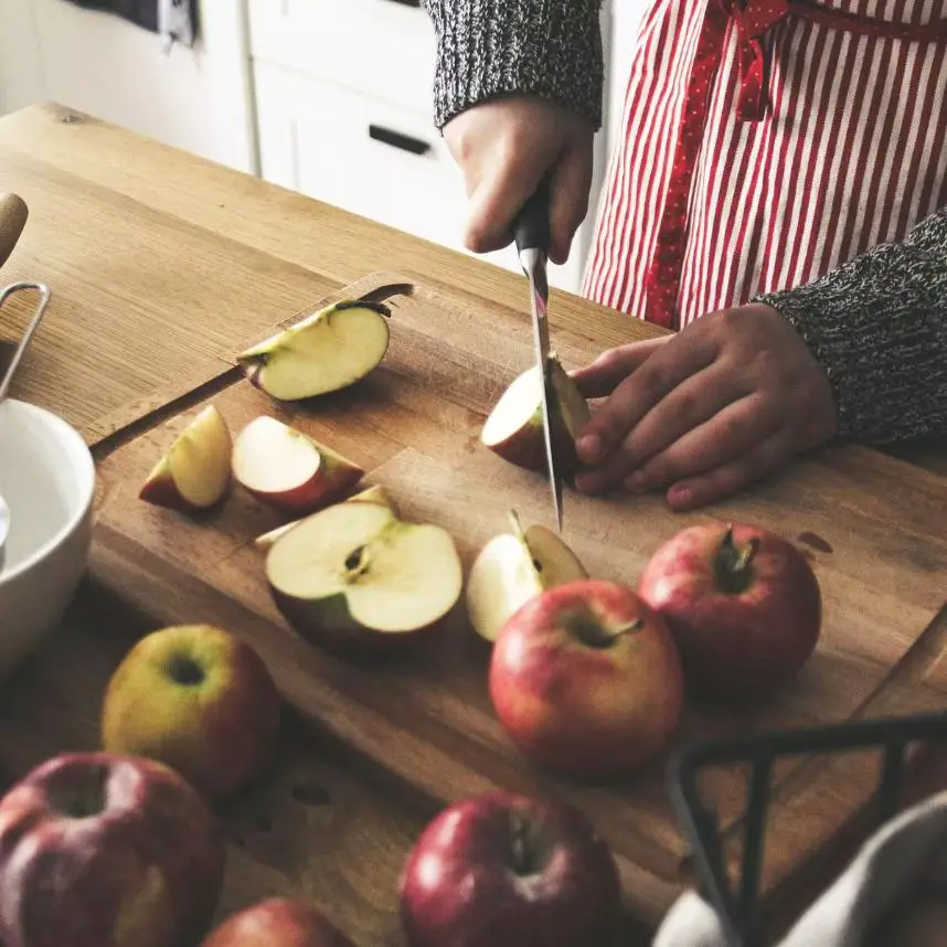 A woman in a red apron carefully slices apples, cutting apples are focused and prominently displayed.