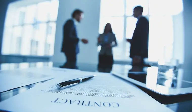 Blurred office scene with three colleagues in discussion, featuring a contact paper prominently placed on a table in the foreground.