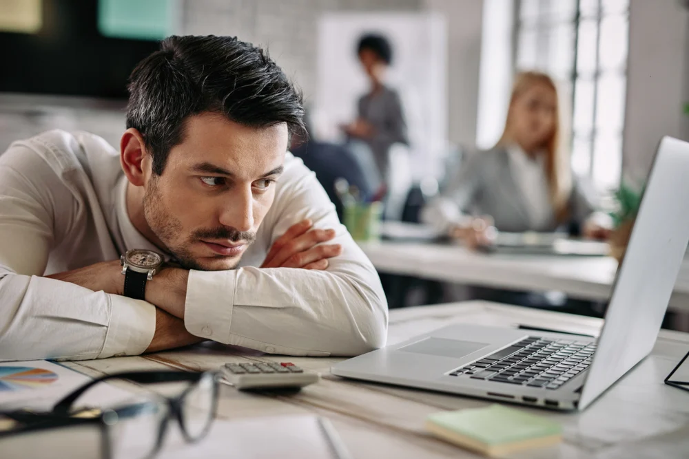Young worker taking a break, looking bored or disengaged while gazing at the screen.