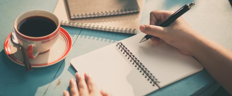 A girl engaged in writing on a notebook, accompanied by a cup of black coffee placed alongside, 