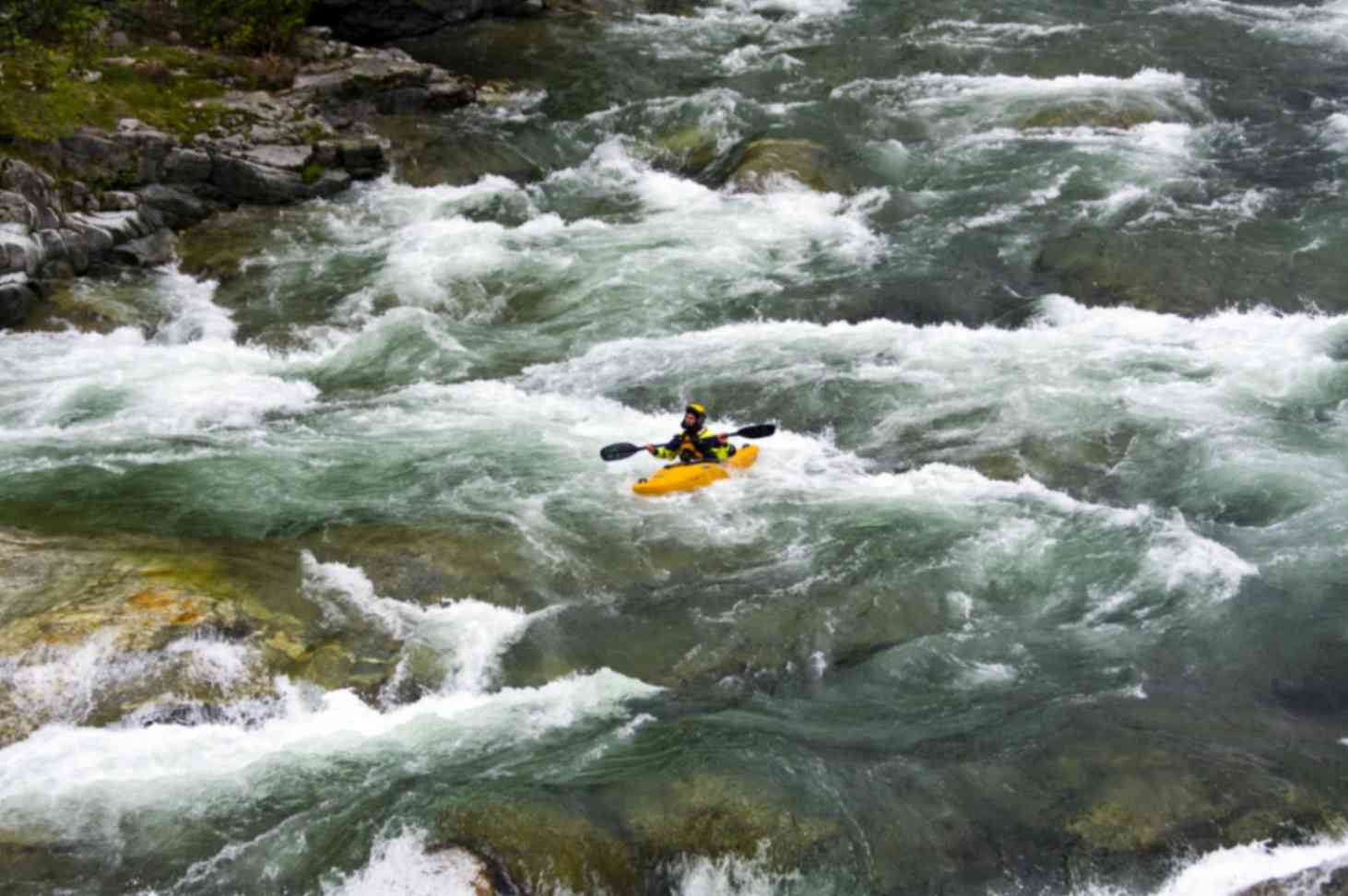 A man rafting in a river stream flowing down huge stone