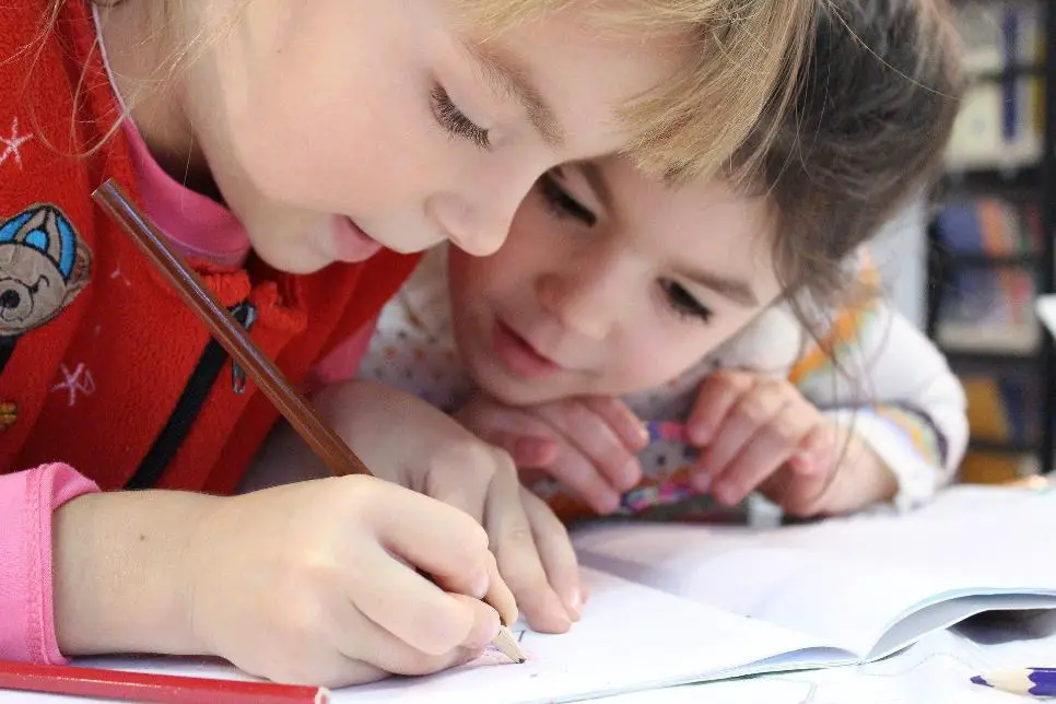 Two little girls, one writing while the other observes attentively.