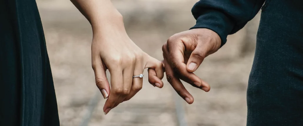 A girl's delicate pinky finger is interwoven with a man's, Girl is wearing a beautiful rings