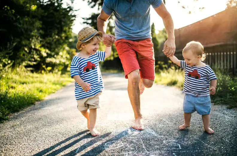 A barefoot man running with two kids, with joyous expressions, on each side, holding their hands tightly as they dash forward. 