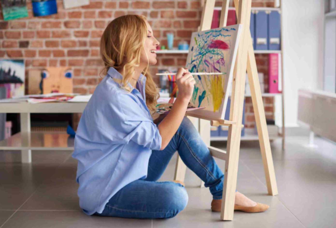 A girl sitting on the floor painting on a canvas