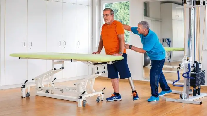 A therapist providing prosthetic training to an elderly man"