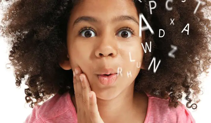 A child with rounded lips tracing various alphabets in the air.