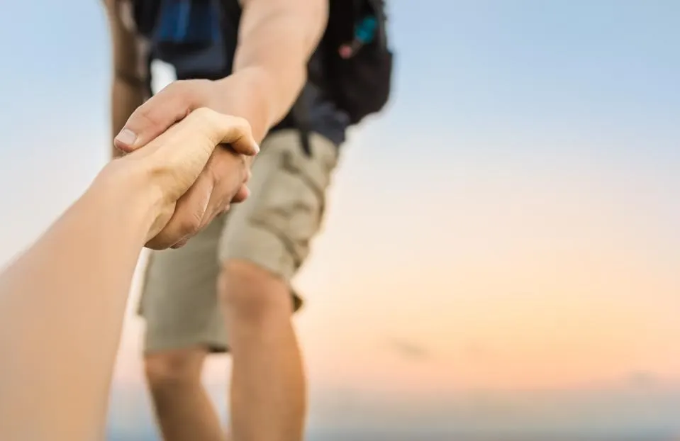 A male hand reaching out to gently grasp a female hand against the backdrop of a hiking scene