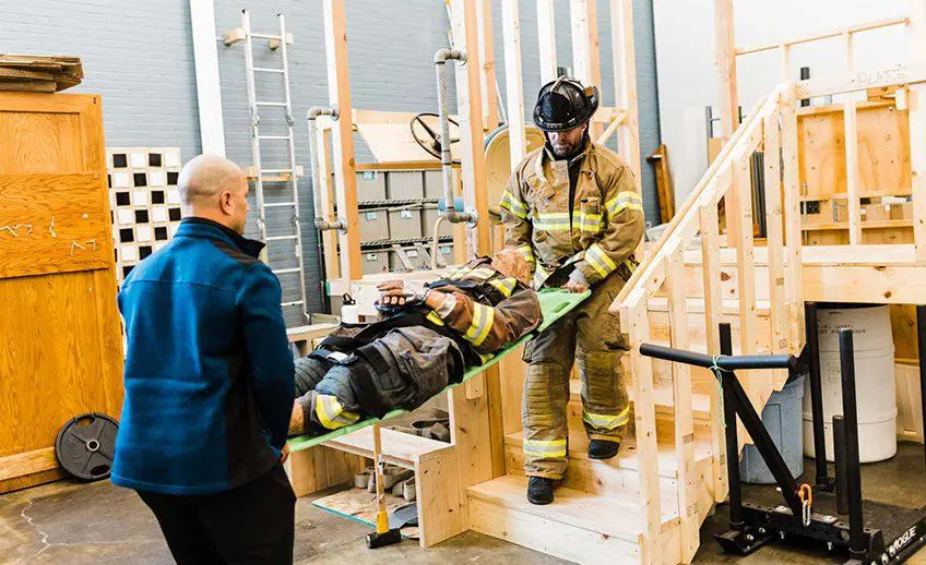 Two men participating in a Work Hardening/Conditioning Program, carrying another person upstairs for stair training