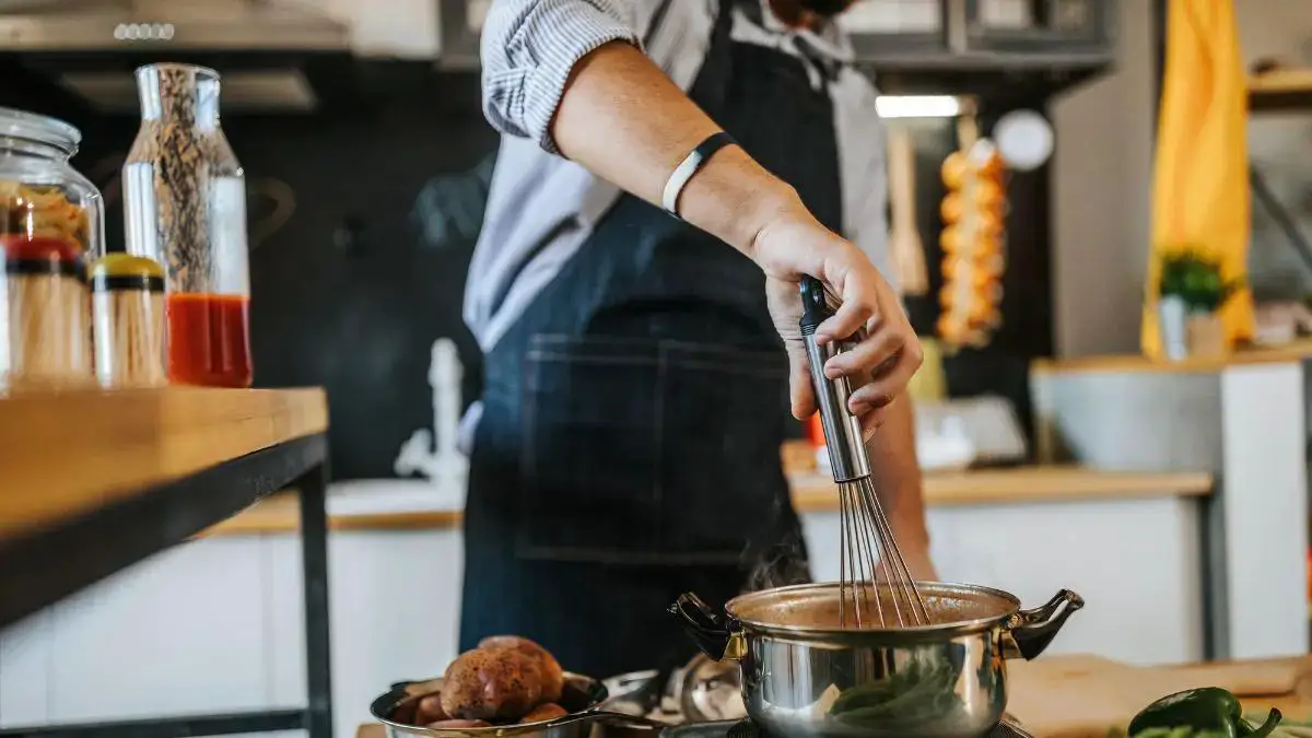 A man standing at a kitchen counter, his head out of view, engaged in the act of cooking.